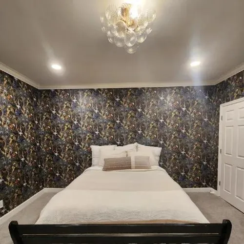Bedroom papered on every wall in a dark multicolor floral print, with a white bed and a bubble-glass ceiling light