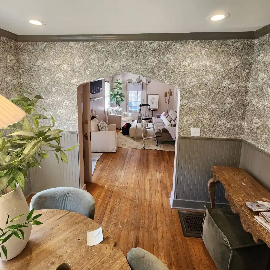 Dining room in a soft gray-green leaf print above gray wainscot, opening through an arch into the living room