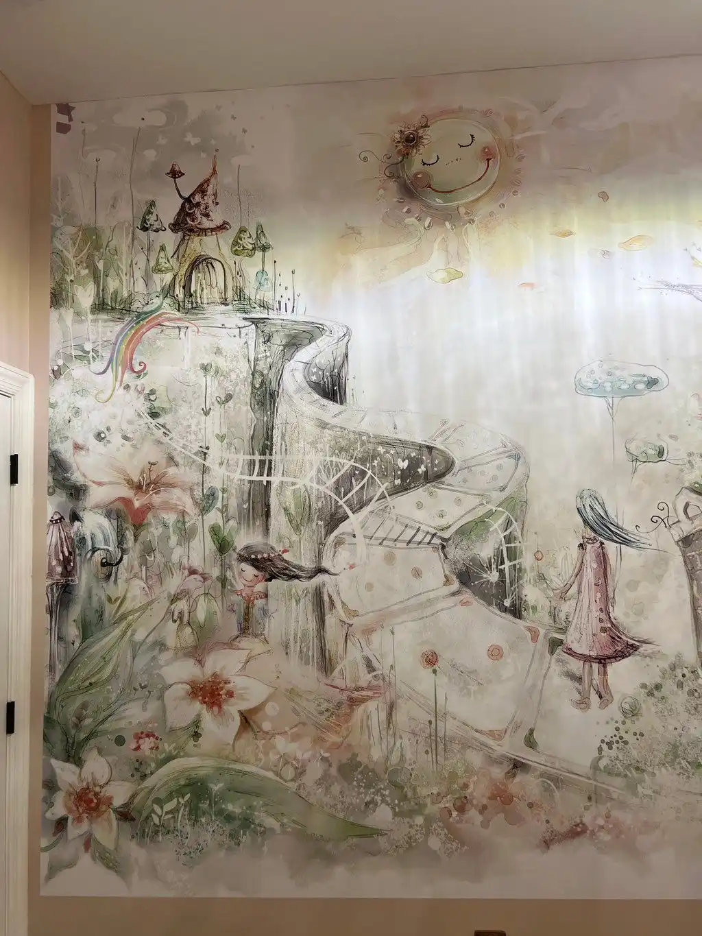 Full-wall painted mural in soft pastels: a fairy-tale landscape with flowers, a winding path and a smiling sun