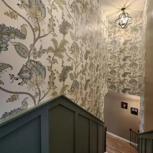 Stairwell papered in a large cream and sage leaf-and-vine print above dark green board-and-batten panels
